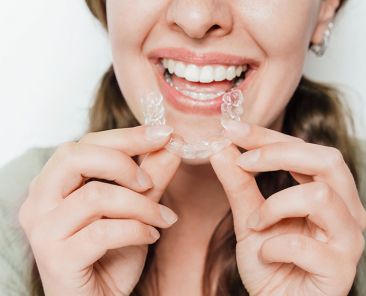 Woman smiling and holding a clear teeth aligner with both hands, dental care and orthodontic treatment aligners